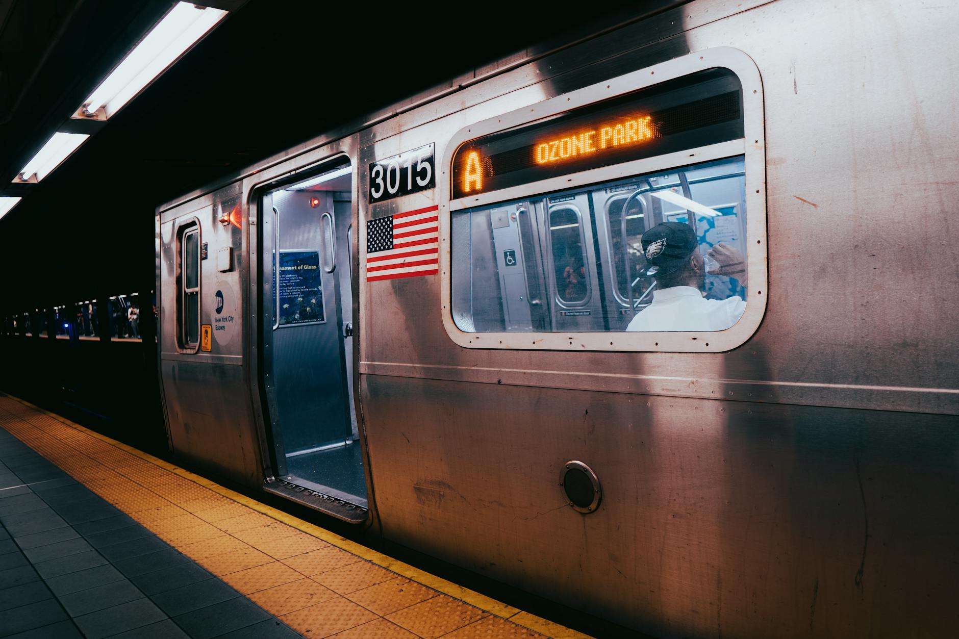 Photo of a subway train at a New York City station at night featuring the American flag and Ozone Park sign.