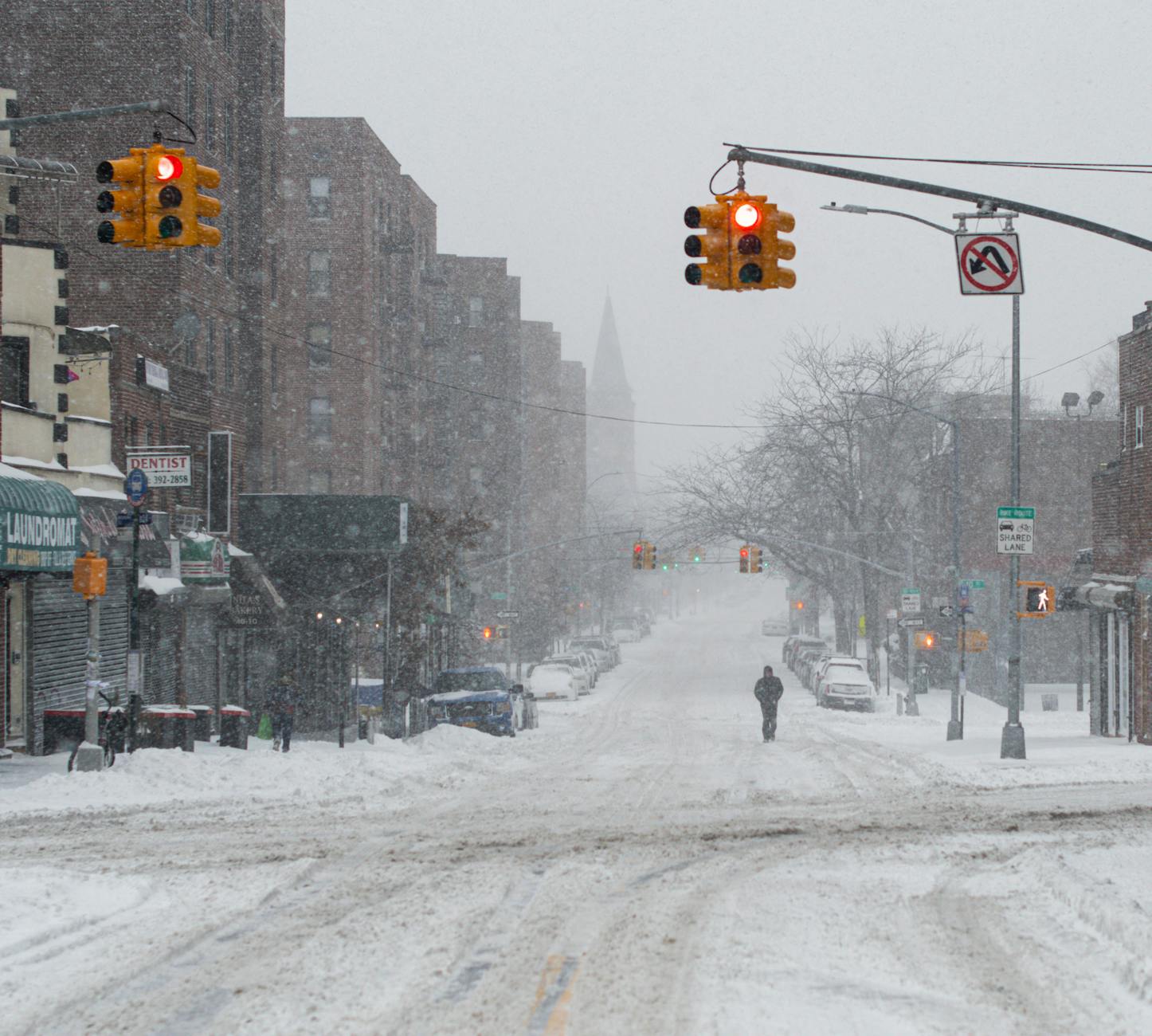 A snow-covered urban street with traffic lights and a lone pedestrian, capturing the essence of winter in the city.